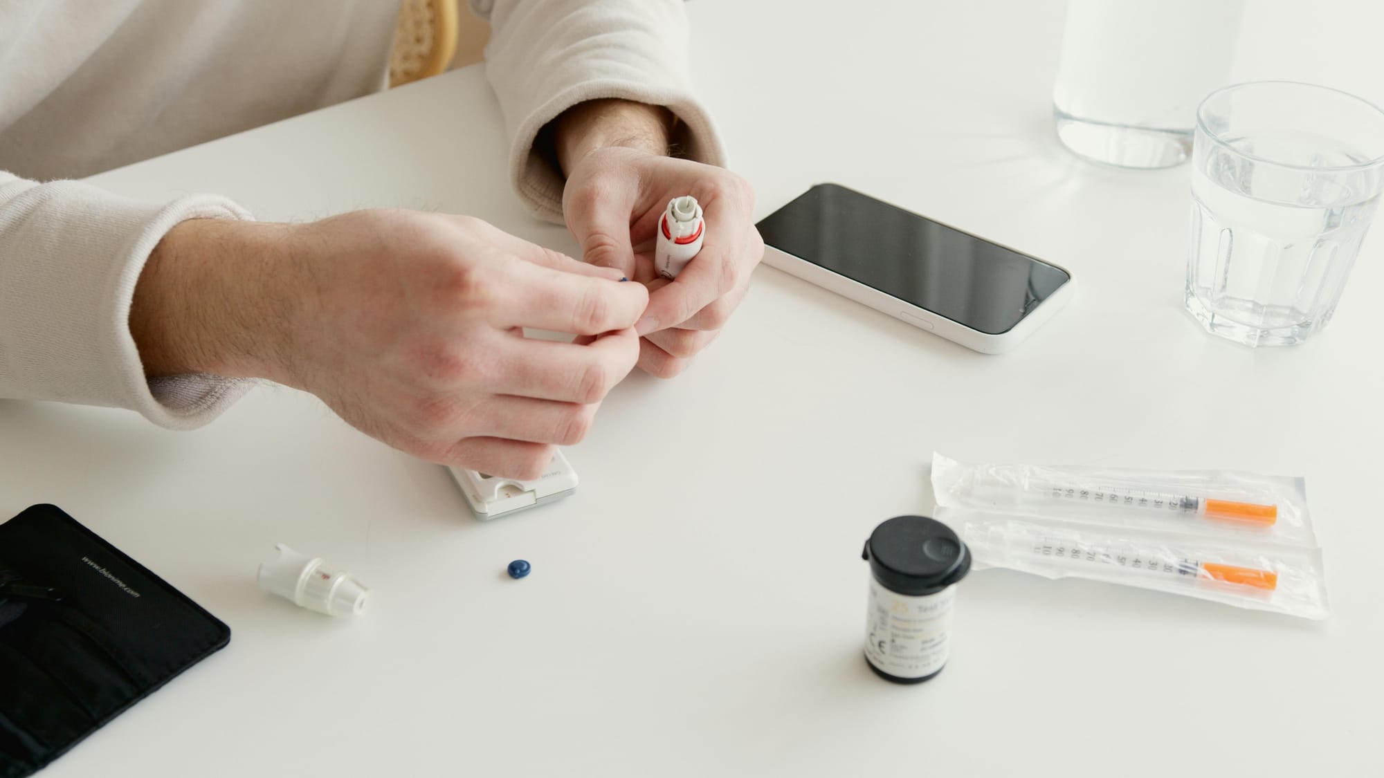 A stock photo of a Caucasian man holding an insulin bottle. in front of him are two needles, an insulin container. to his left are two glasses of water.